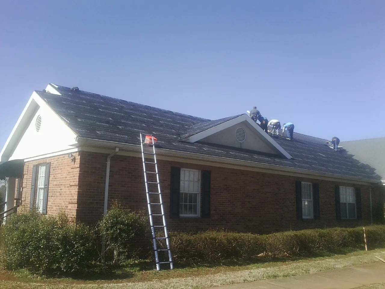 Crew tearing shingles off a brick ranch roof with a ladder set — Metal Roof Repair work by our crew in Sumner